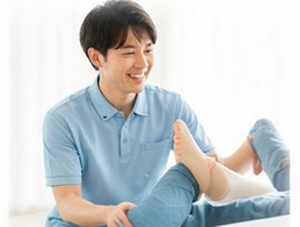 脚の関節を動かすリハビリを行う男性スタッフ