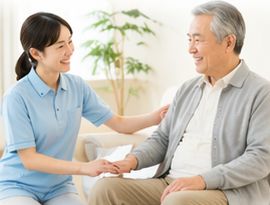 自宅のソファで高齢男性の手に触れるスタッフ